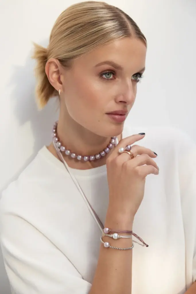 Blonde Dame mit weißem Shirt trägt einen Ring, zwei Ketten und zwei Armbänder von GELLNER